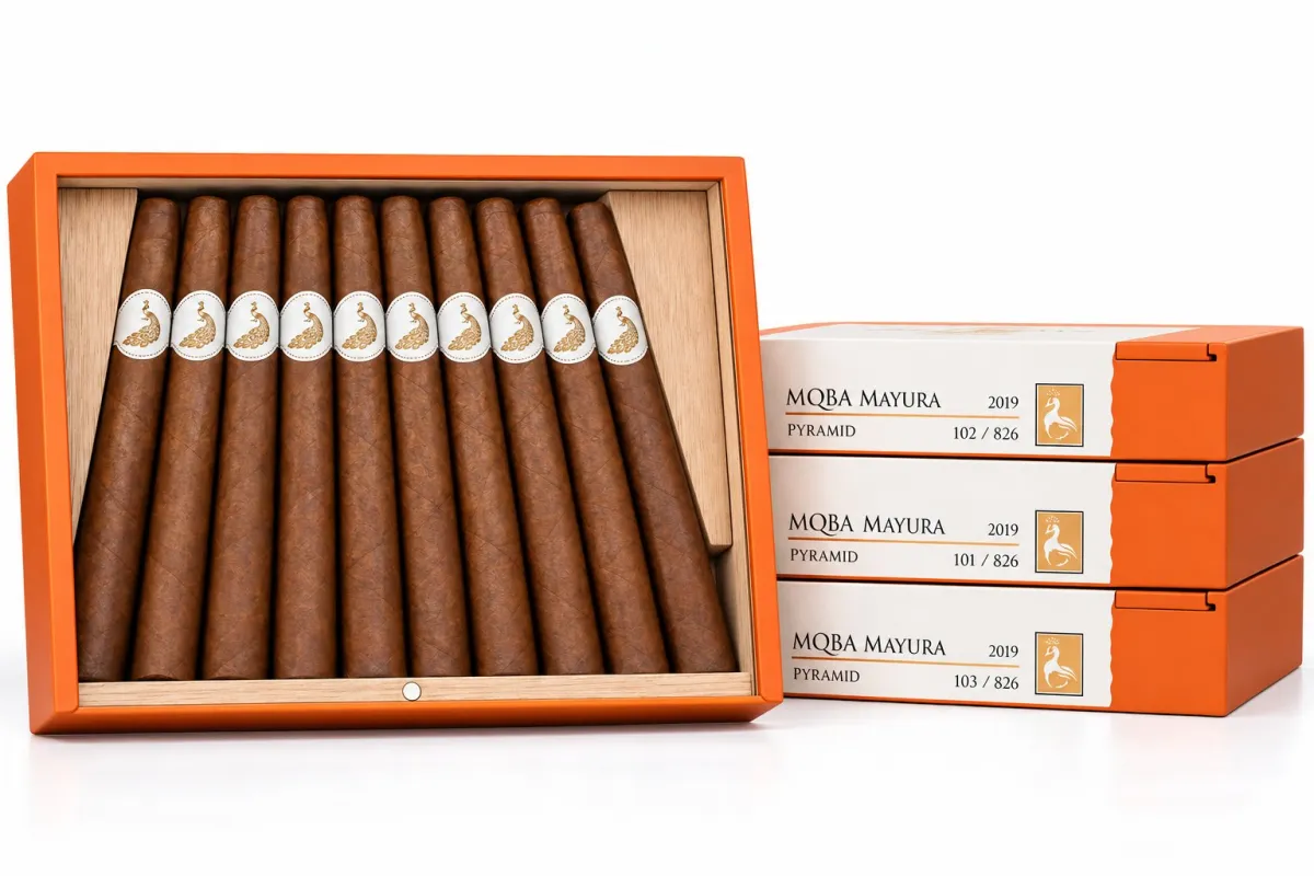 Open orange box of ten MBombay MQBA Mayura Pyramid 2019 cigars with white oval gold peacock bands, beside three stacked box sleeves numbered out of 826