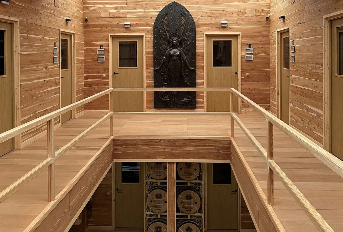 Cedar-paneled atrium lined with doors to aging rooms, with a bronze sculpture at the far end, inside Selected Tobacco's Madrid facility