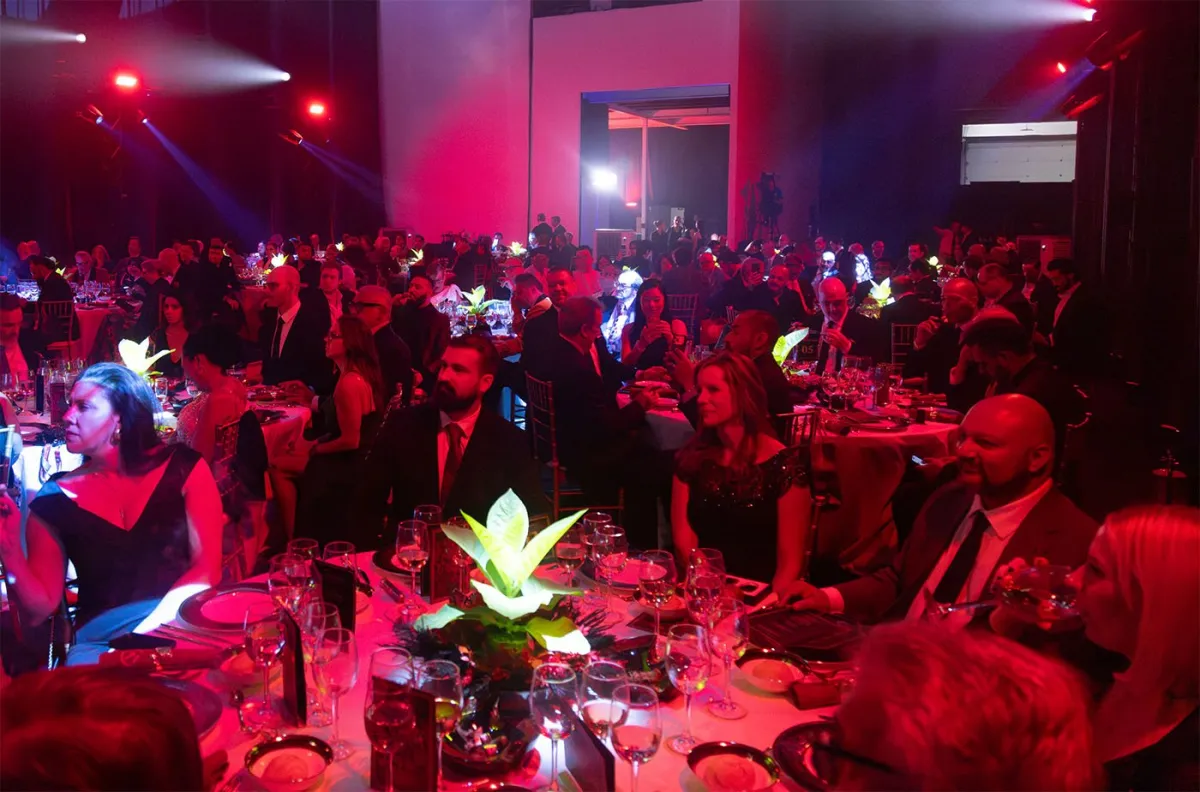 Crowded gala dinner under red lights with tobacco plant centerpieces at the Selected Tobacco grand opening in Madrid