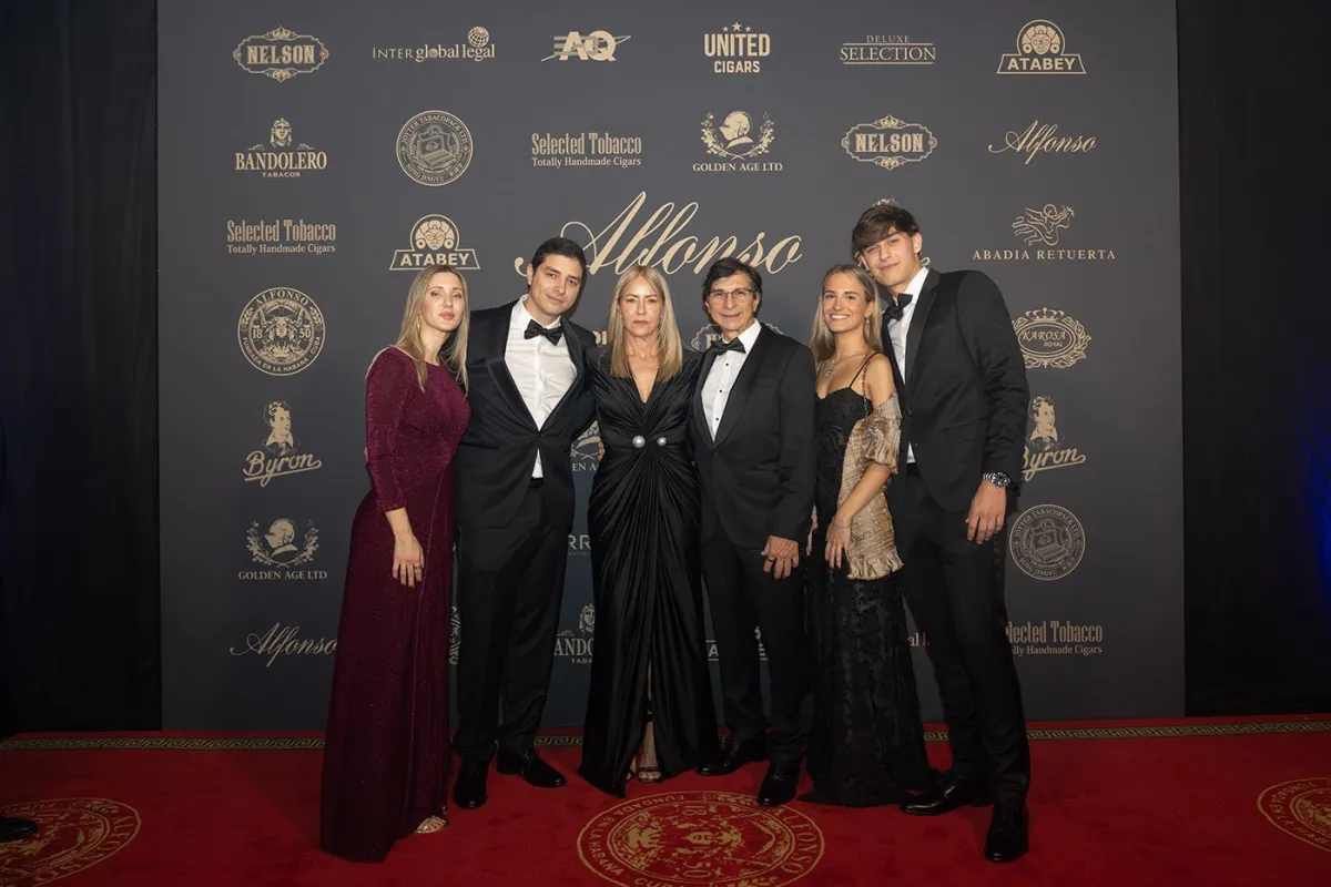 A group in formal wear posing in front of a Selected Tobacco brand backdrop at the Madrid grand opening gala