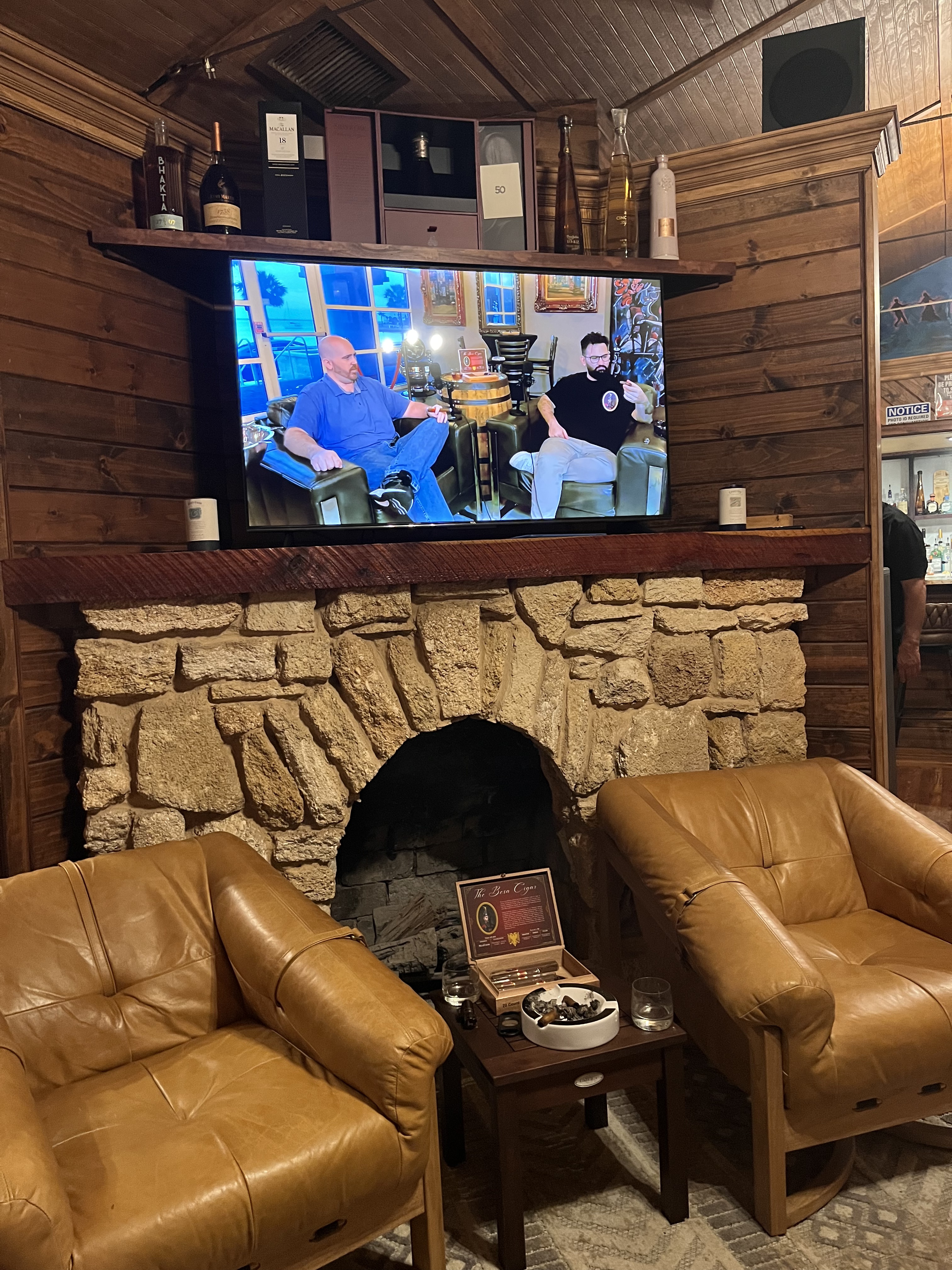 The Cigar Guys Podcast playing on a TV above a fireplace at Jefe Cigar Lounge